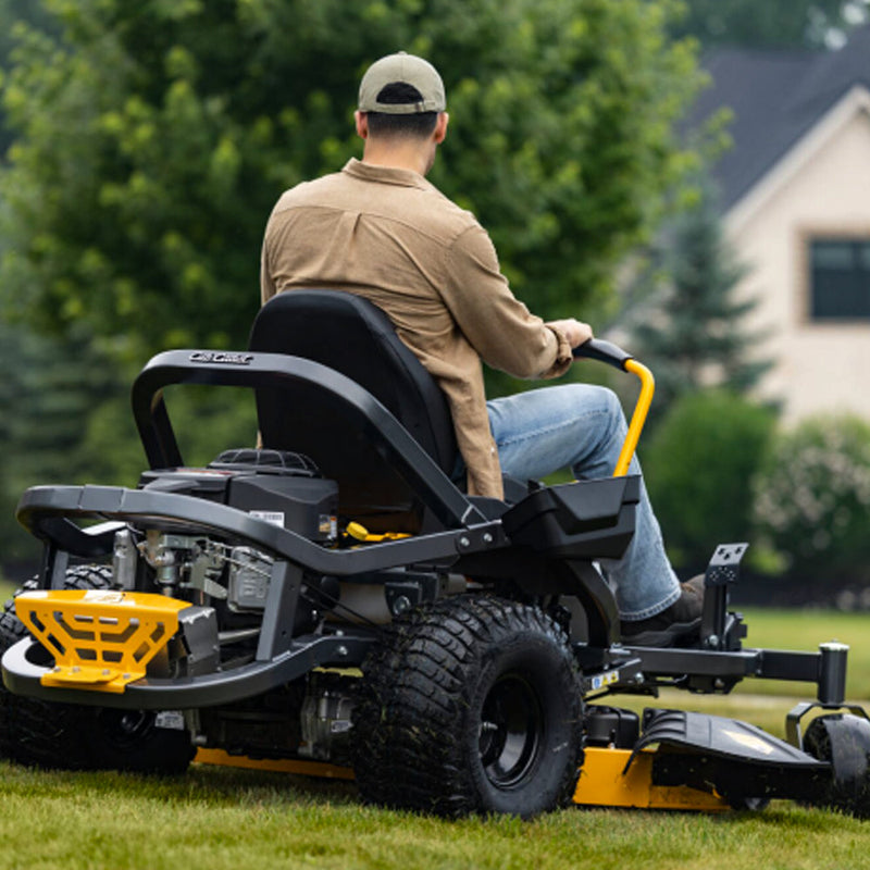 A man wearing a tan shirt, blue jeans, and a baseball cap sits on a Cub Cadet Ultima Z2 46 zero-turn lawn mower, viewed from behind as he drives it across a green lawn. Cub Cadet available Mower City labuty Wodonga