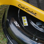 Close-up of a black and yellow Cub Cadet lawn mower deck, showing the 'Cub Cadet' logo, a '30"' size sticker, and safety warning labels. CC30 HX Mini Rider. Talk to the Team at Mower City Albury