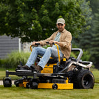 A man wearing a beige cap, tan shirt, and blue jeans sits on a Cub Cadet Ultima Z2 46 zero-turn mower cutting green grass in a backyard with trees in the background. Cub Cadet available at Mower City Albury Wodonga